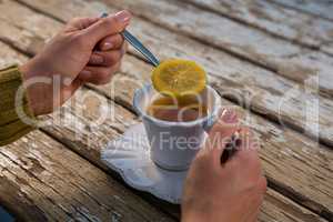 Cropped hands of woman holding lemon in spoon while having tea