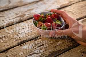 Cropped hand holding bowl containing strawberries