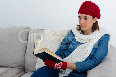 Woman reading book while sitting on sofa