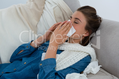 Young woman rubbing nose while lying on sofa