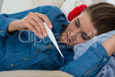 Woman checking thermometer while lying on sofa