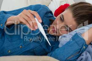 Woman checking thermometer while lying on sofa