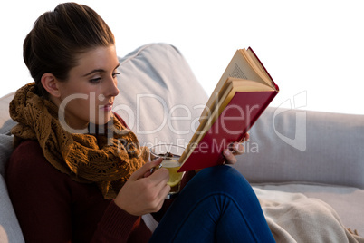 Young woman reading book while having tea