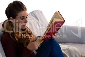 Young woman reading book while having tea