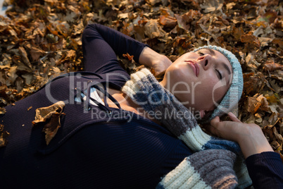 Close up of woman with hands behind head lying on dry leaves