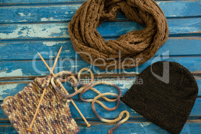 High angle view of muffler with knit hat and knitting needles