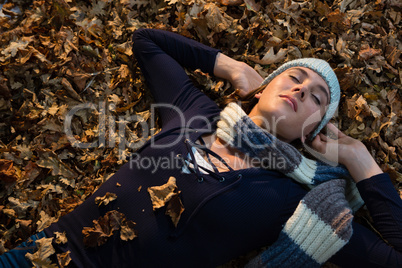 High angle view of woman with hands behind head lying on dry leaves