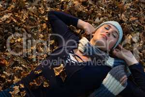 High angle view of woman with hands behind head lying on dry leaves