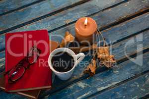 High angle view of tea cup with eyeglasses and books by illuminated candle