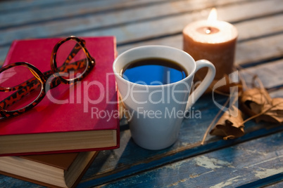 Close up of tea cup with eyeglasses and books by illuminated candle