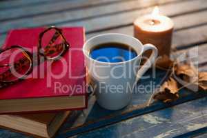 Close up of tea cup with eyeglasses and books by illuminated candle