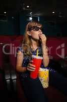 Girl wearing 3D glasses while eating popcorn during movie