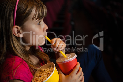 Side view of girl having drink and popcorn during movie