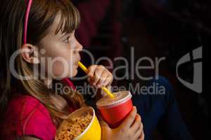 Side view of girl having drink and popcorn during movie
