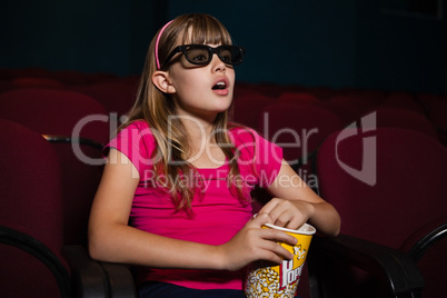 Surprised girl using 3D glasses while having popcorns during movie