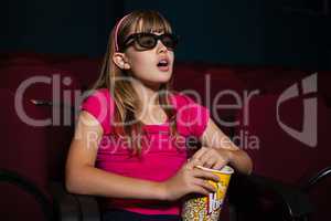 Surprised girl using 3D glasses while having popcorns during movie