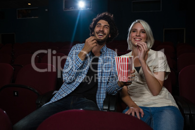 Couple having popcorn while watching movie in theatre