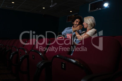 Couple having popcorn while watching movie in theatre