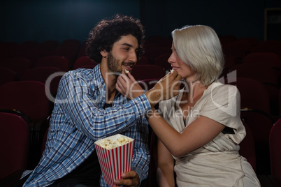 Couple feeding popcorn to each other while sitting in theatre