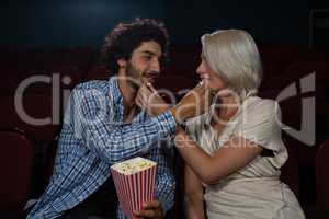 Couple feeding popcorn to each other while sitting in theatre