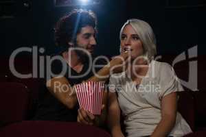 Couple having popcorn while watching movie in theatre