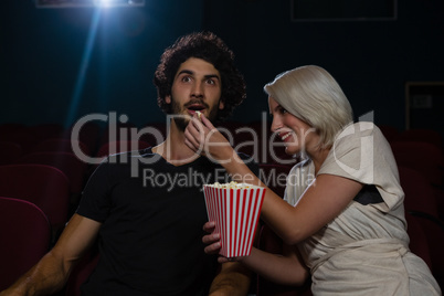 Couple having popcorn while watching movie in theatre