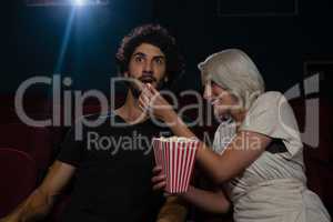 Couple having popcorn while watching movie in theatre