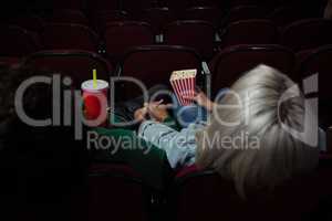 Couple having popcorn while watching movie in theatre