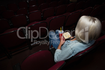 Woman having popcorn while watching movie in theatre