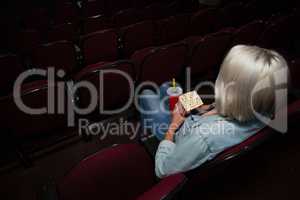 Woman having popcorn while watching movie in theatre