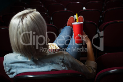 Woman having drinks while watching movie in theatre