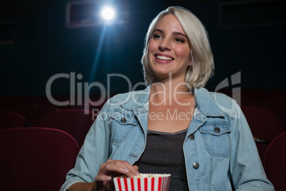 Woman having popcorn while watching movie in theatre