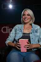 Woman having popcorn while watching movie in theatre