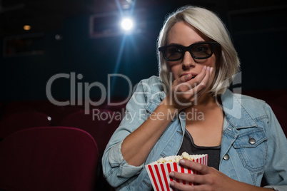 Woman having popcorn while watching movie in theatre