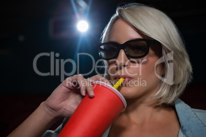 Woman drinking cold drink while watching movie in theatre