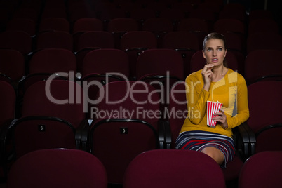 Woman having popcorn while watching movie in theatre