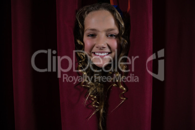 Smiling female artist peeking through the red curtain