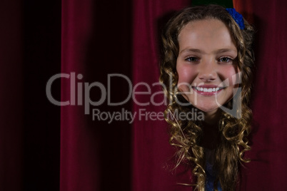 Smiling female artist peeking through the red curtain