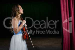 Thoughtful woman with violin standing on stage