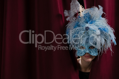 Female artist in masquerade mask peeking through the red curtain