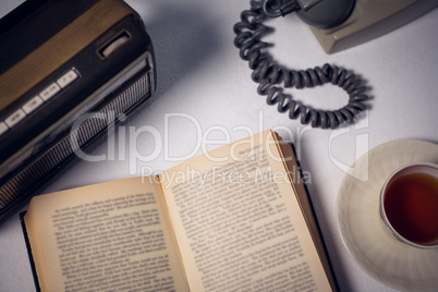 Overhead view of book with tea and telephone by radio