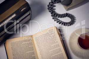 Overhead view of book with tea and telephone by radio