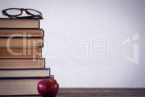 Apple by stack of book with eyeglass at table