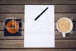 Overhead view of coffee cup with fountain pen on paper by donut