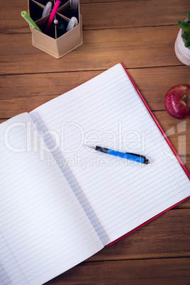 Overhead view of book with pen and apple by houseplant