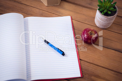 Book with pen and apple by houseplant