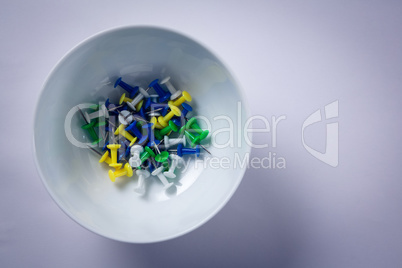Various push pins in bowl on white background