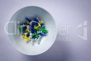 Various push pins in bowl on white background