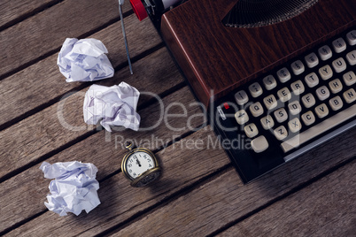 Vintage typewriter, pocket watch and crumbled paper on wooden table