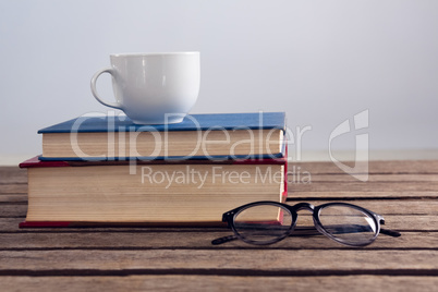 Books with cup of coffee and spectacles on wooden table